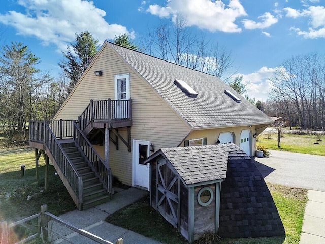 view of home's exterior with a deck, stairway, a shingled roof, and a garage