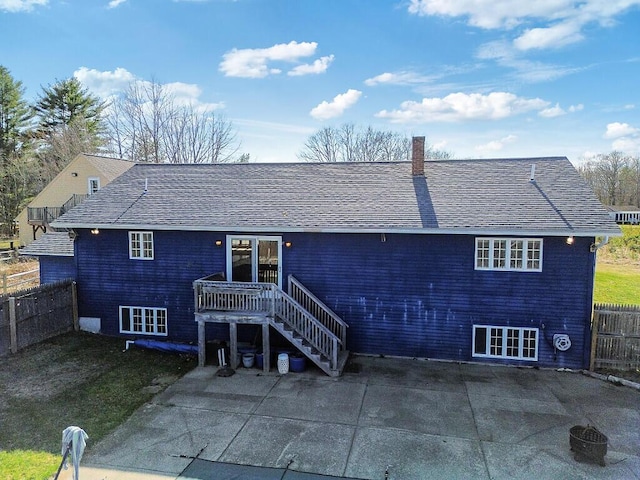 rear view of property featuring fence, roof with shingles, a chimney, and a patio