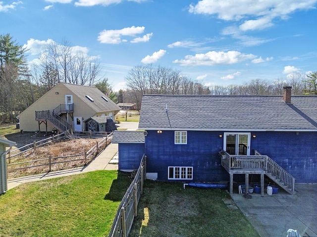 back of house featuring a chimney, roof with shingles, stairway, a yard, and fence private yard