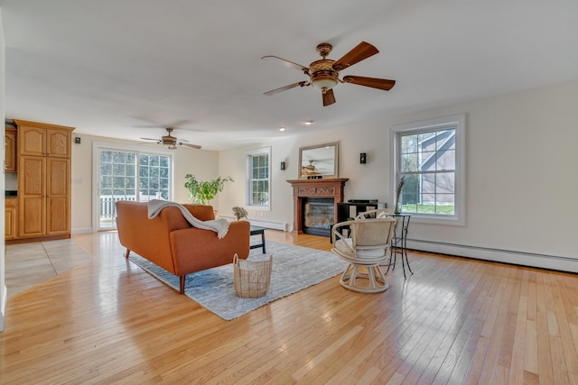 living room featuring ceiling fan, baseboard heating, light wood-style flooring, and a glass covered fireplace
