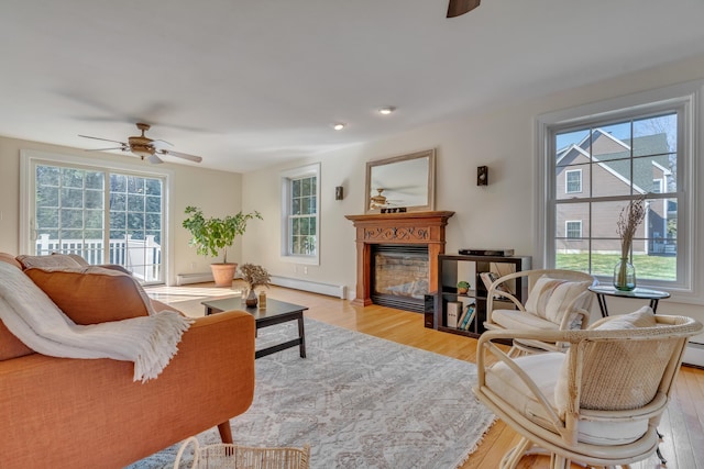 living area with a wealth of natural light, a ceiling fan, and a baseboard heating unit