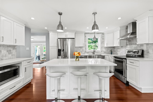 kitchen featuring tasteful backsplash, a breakfast bar, stainless steel appliances, a sink, and wall chimney exhaust hood