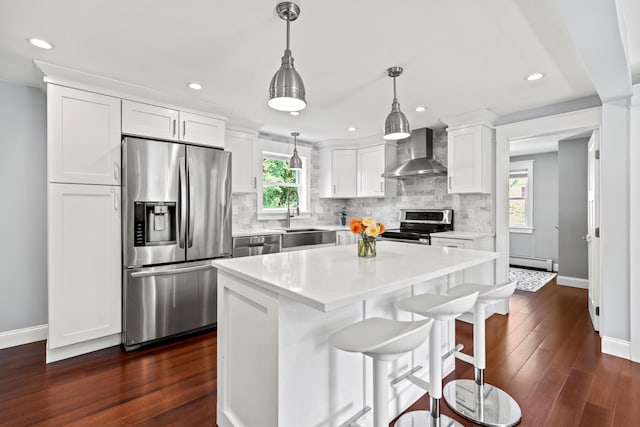 kitchen with wall chimney range hood, stainless steel appliances, baseboard heating, and baseboards