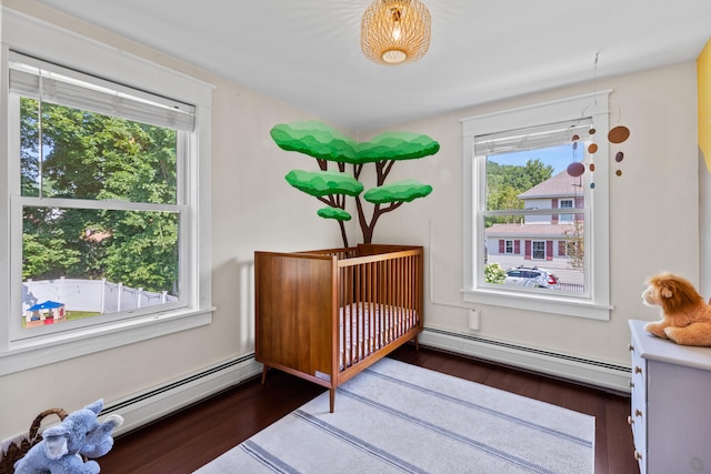 bedroom featuring a crib, wood finished floors, and a baseboard heating unit