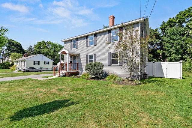 colonial-style house featuring a front yard, fence, a gate, and a chimney