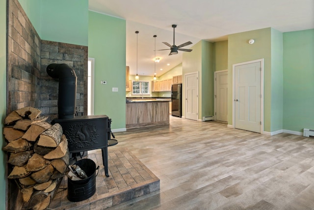 living room featuring baseboards, a wood stove, light wood-type flooring, and a ceiling fan