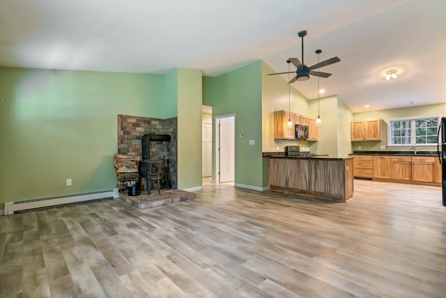 unfurnished living room with light wood-style flooring, a baseboard heating unit, ceiling fan, a wood stove, and high vaulted ceiling