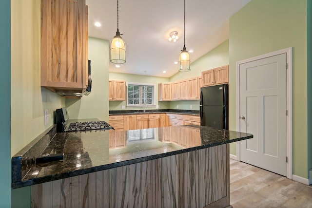 kitchen featuring light brown cabinets, freestanding refrigerator, a sink, a peninsula, and range with gas stovetop