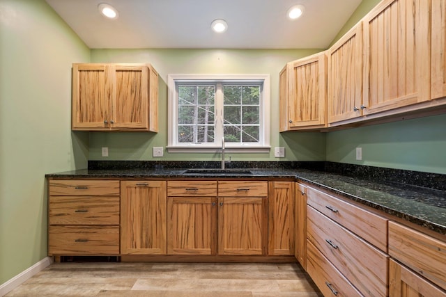 kitchen featuring dark stone counters, light wood finished floors, recessed lighting, and a sink