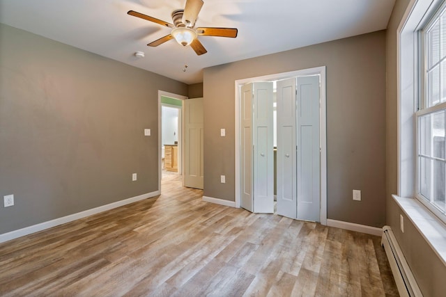 unfurnished bedroom with a ceiling fan, light wood-style flooring, baseboard heating, and baseboards