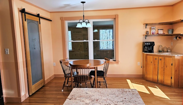 dining area with wood finished floors, crown molding, baseboards, and a barn door