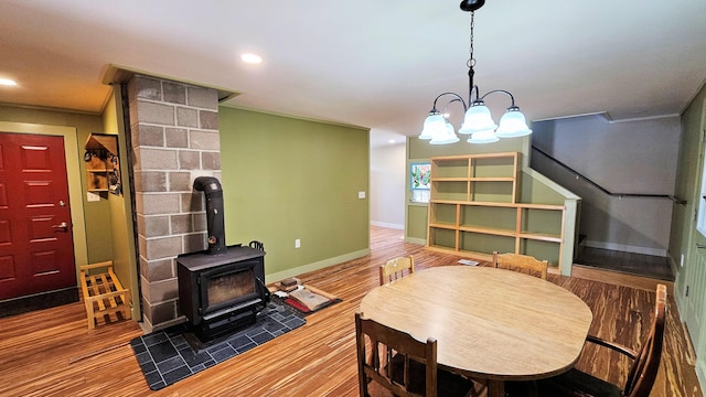 dining space featuring crown molding, a wood stove, a chandelier, baseboards, and wood finished floors
