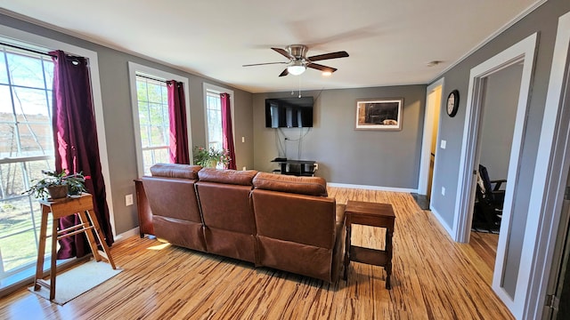 living room with crown molding, a ceiling fan, baseboards, and light wood-style floors