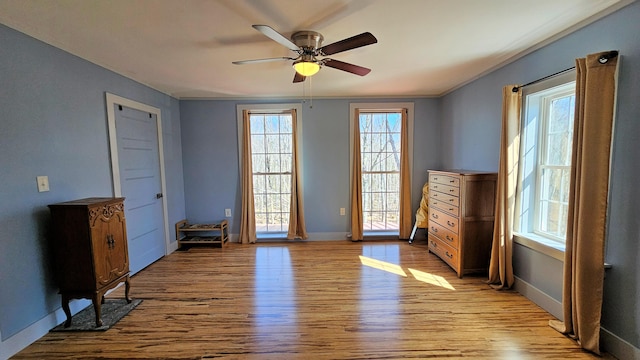 interior space with wood finished floors, ceiling fan, crown molding, and baseboards
