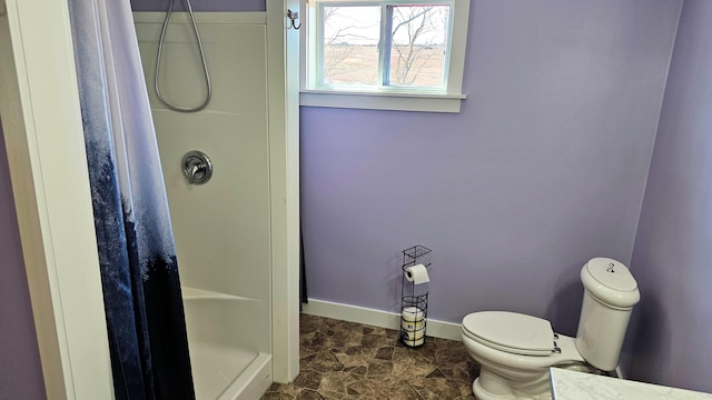 bathroom featuring toilet, a stall shower, and baseboards