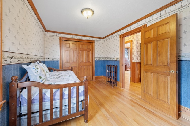bedroom with crown molding, wainscoting, wallpapered walls, and wood finished floors