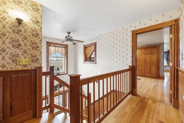 hall with light wood finished floors, an upstairs landing, and wallpapered walls