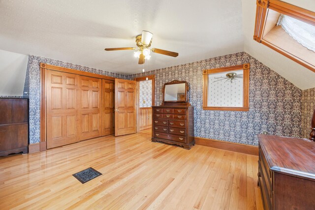 bedroom with light wood-style flooring, a ceiling fan, baseboards, wallpapered walls, and visible vents