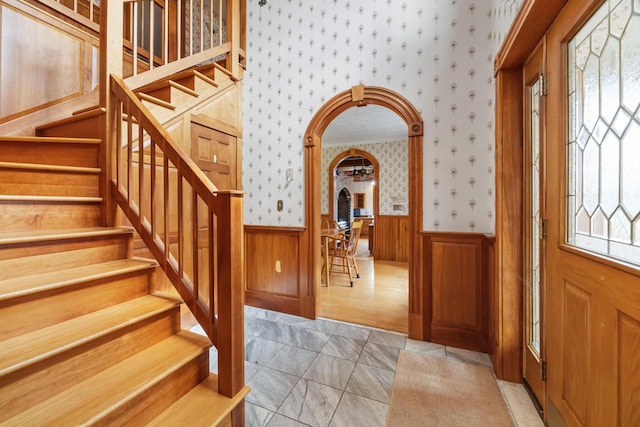 entrance foyer featuring arched walkways, wallpapered walls, wainscoting, and stairway