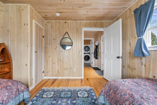 bedroom featuring stacked washer / dryer, wood finished floors, wooden walls, and wood ceiling