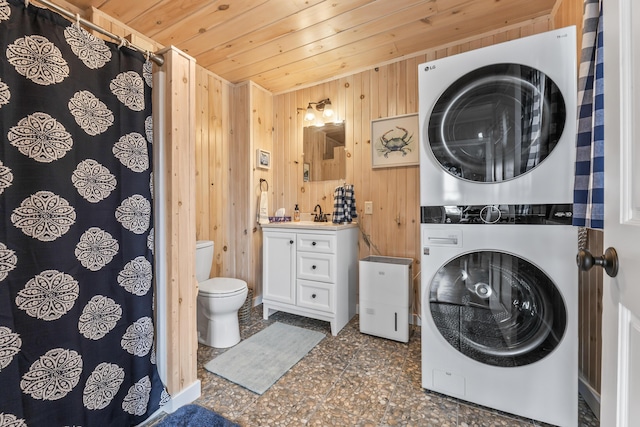 clothes washing area featuring stacked washer / drying machine, a sink, laundry area, wooden walls, and wood ceiling