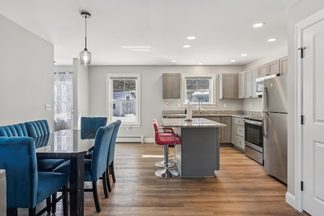 kitchen featuring plenty of natural light, a baseboard heating unit, a kitchen bar, and stainless steel appliances