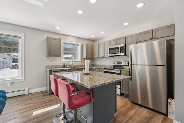 kitchen featuring plenty of natural light, appliances with stainless steel finishes, a baseboard heating unit, and a kitchen bar