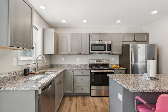 kitchen featuring light stone countertops, appliances with stainless steel finishes, a sink, light wood-style floors, and recessed lighting
