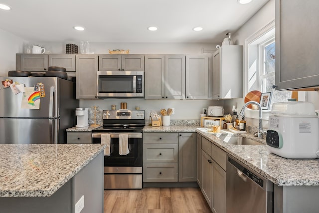 kitchen featuring light stone counters, appliances with stainless steel finishes, a sink, light wood-style floors, and recessed lighting