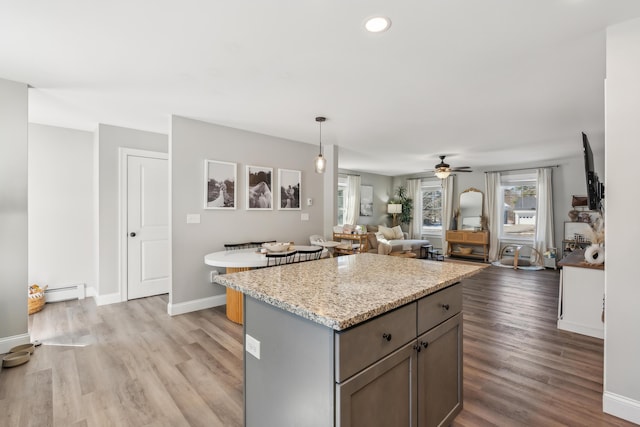 kitchen with light wood-type flooring, a ceiling fan, a baseboard heating unit, and a kitchen island