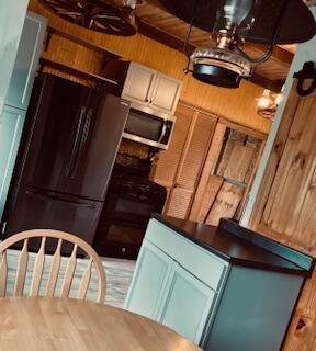 kitchen featuring wooden walls, dark countertops, stove, freestanding refrigerator, and stainless steel microwave