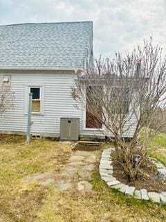 back of house with a lawn, central air condition unit, and a shingled roof