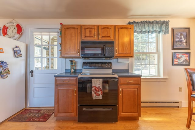 kitchen with light wood finished floors, black appliances, dark countertops, baseboard heating, and plenty of natural light