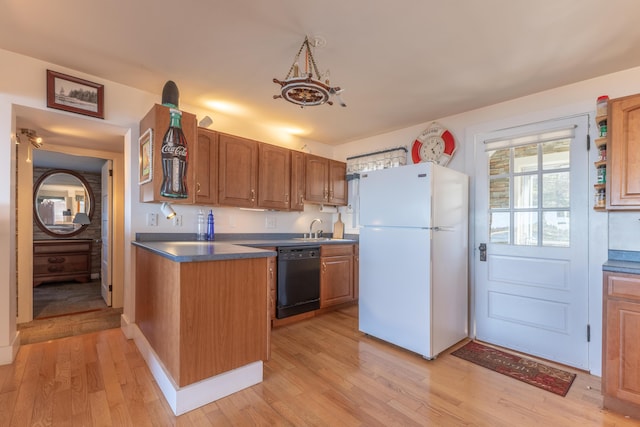 kitchen featuring freestanding refrigerator, black dishwasher, dark countertops, light wood finished floors, and a sink