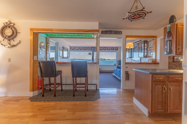 kitchen featuring baseboards, brown cabinetry, dark countertops, and light wood-style floors