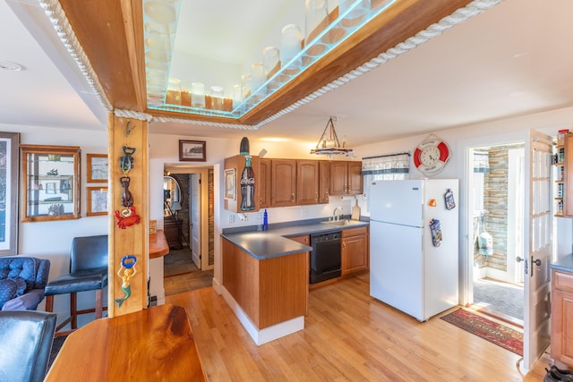 kitchen featuring freestanding refrigerator, black dishwasher, dark countertops, light wood finished floors, and a sink