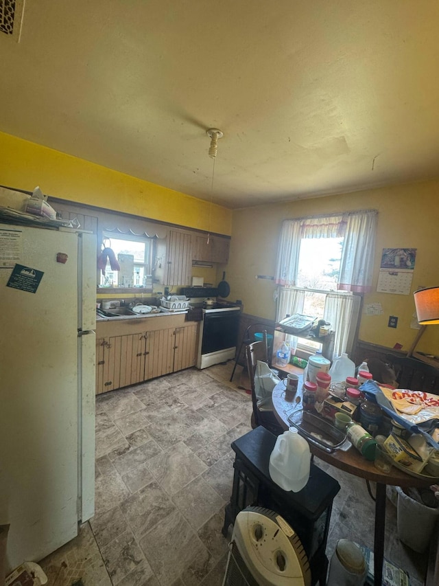 kitchen with stone finish flooring, freestanding refrigerator, light brown cabinets, visible vents, and electric stove