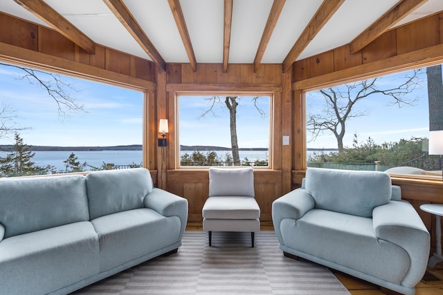 living area with a water view, lofted ceiling with beams, and wood walls