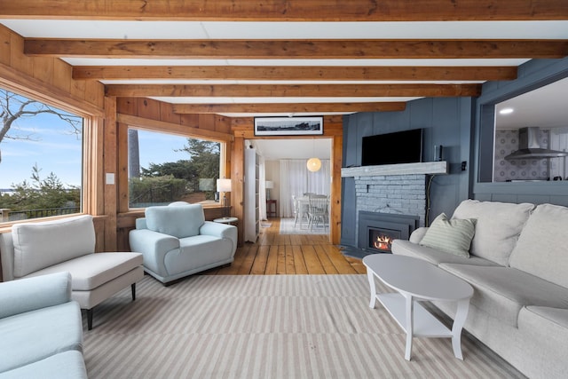living area featuring wooden walls, beamed ceiling, a brick fireplace, and hardwood / wood-style floors