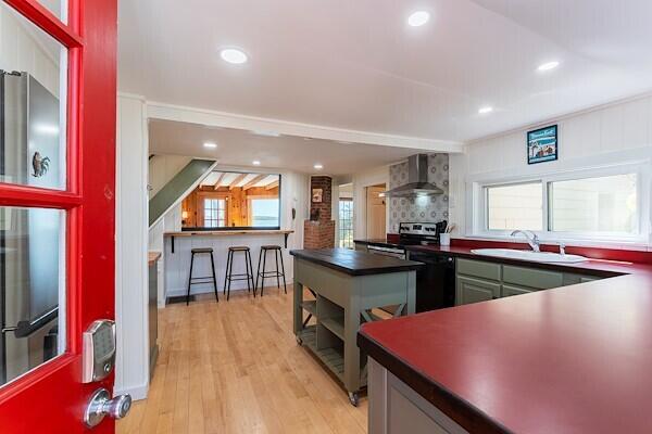 kitchen with dark countertops, black dishwasher, wall chimney range hood, a sink, and stainless steel electric range oven
