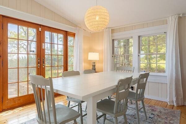 dining space with light wood-style flooring, a notable chandelier, french doors, and lofted ceiling