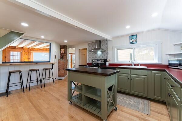 kitchen with wall chimney range hood, dark countertops, open shelves, and stainless steel appliances