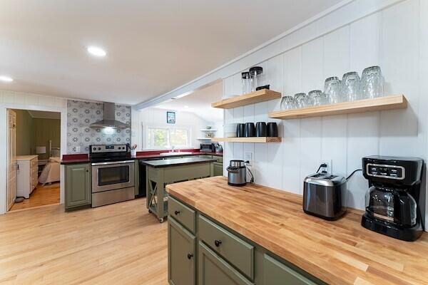 kitchen featuring open shelves, butcher block countertops, wall chimney exhaust hood, gray cabinets, and stainless steel range with electric cooktop