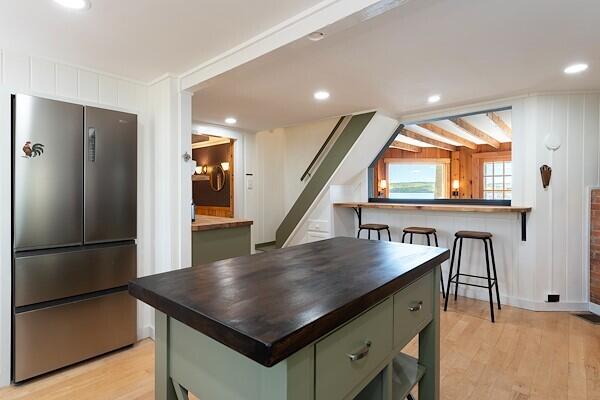 kitchen featuring green cabinetry, butcher block countertops, light wood-style flooring, freestanding refrigerator, and recessed lighting