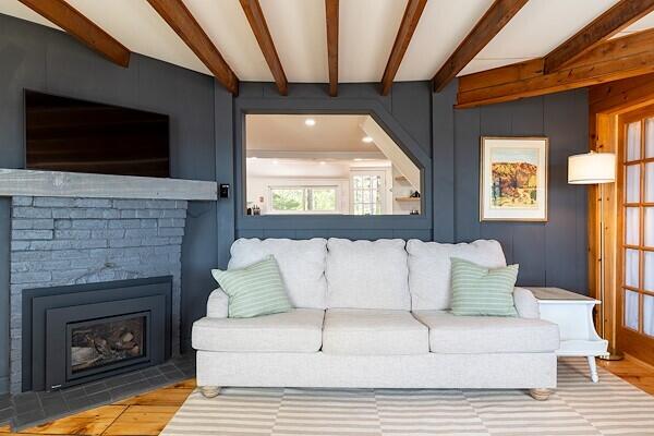 living room featuring beamed ceiling, a fireplace with flush hearth, and wood finished floors