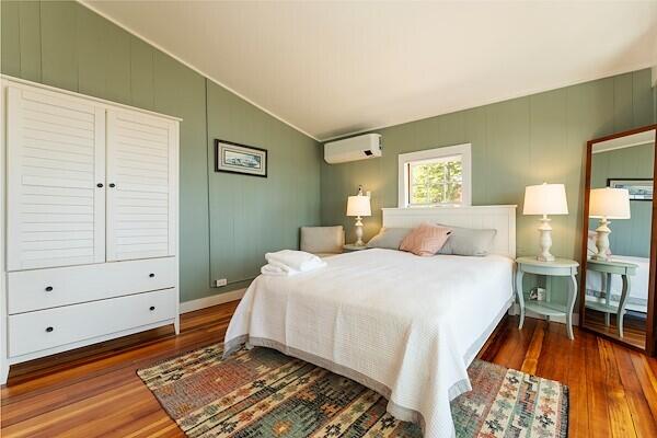 bedroom featuring wood finished floors, lofted ceiling, a wall unit AC, and a decorative wall