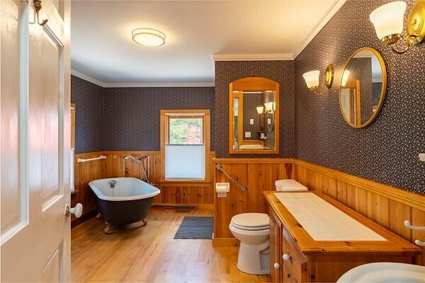 bathroom with wainscoting, a freestanding tub, ornamental molding, and wood finished floors