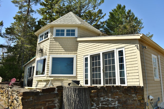 view of property exterior featuring a shingled roof and stone siding