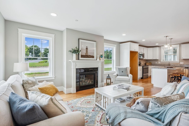 living room featuring a glass covered fireplace, recessed lighting, light wood-style flooring, and baseboards