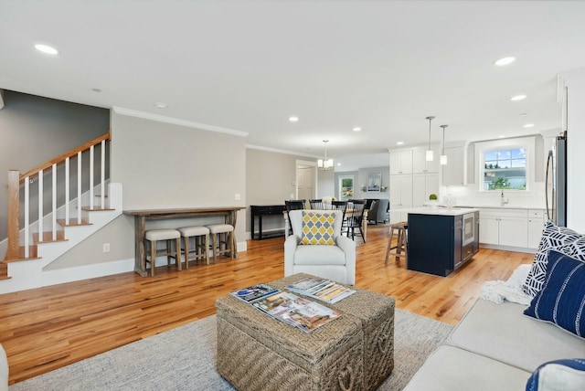 living room featuring recessed lighting, light wood-style floors, crown molding, and stairway